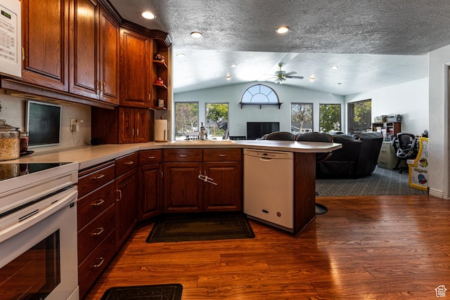 kitchen featuring lofted ceiling, dark wood-style floors, a sink, white appliances, and a peninsula