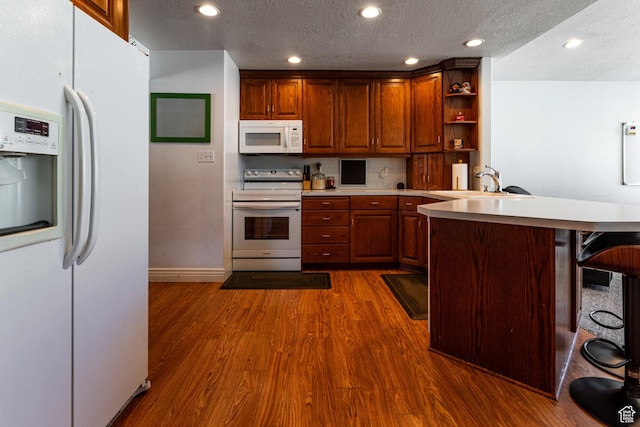 kitchen featuring a sink, a textured ceiling, white appliances, a peninsula, and dark wood-style floors