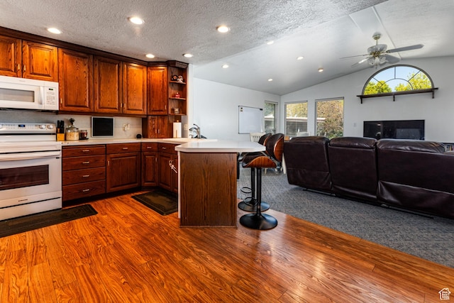 kitchen featuring open floor plan, a breakfast bar, white appliances, a peninsula, and dark wood-style flooring