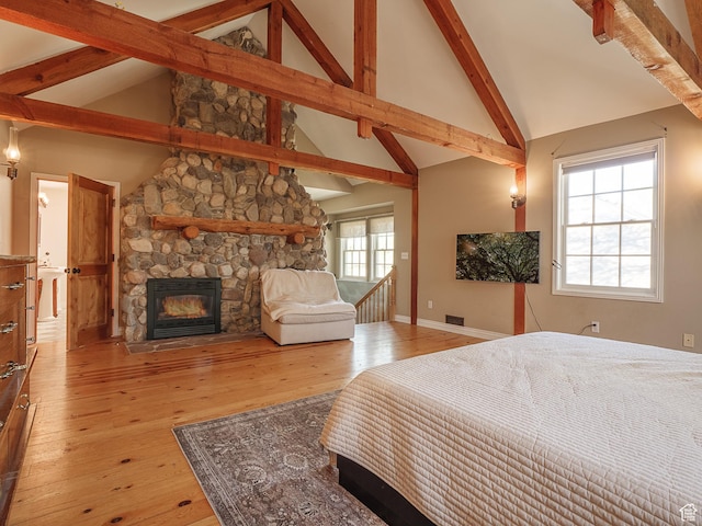 bedroom featuring a stone fireplace, light wood-style floors, beam ceiling, baseboards, and high vaulted ceiling