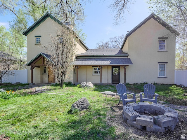 back of property with fence, an outdoor fire pit, a yard, and stucco siding
