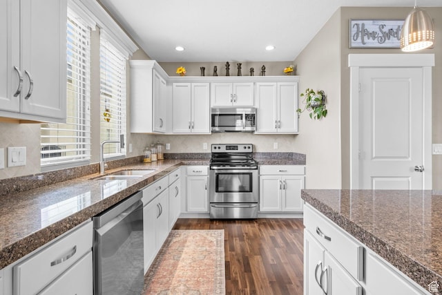 kitchen with a sink, hanging light fixtures, white cabinetry, dark wood finished floors, and appliances with stainless steel finishes