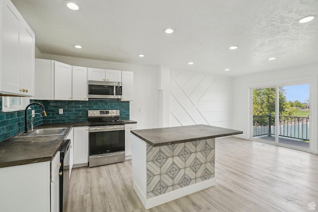 kitchen featuring a sink, decorative backsplash, dark countertops, stainless steel appliances, and light wood-type flooring