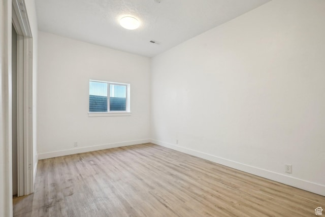 empty room featuring light wood-type flooring, visible vents, and baseboards