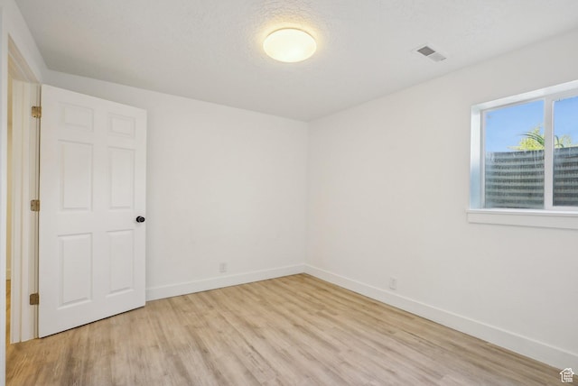 empty room featuring light wood finished floors, baseboards, and visible vents