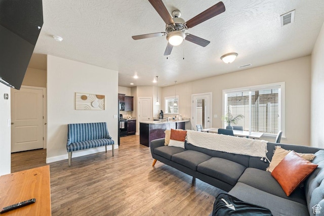 3030 N 125 E, Cedar City, UT 84721 - living room featuring light wood-style flooring, a textured ceiling, baseboards, visible vents, and a ceiling fan