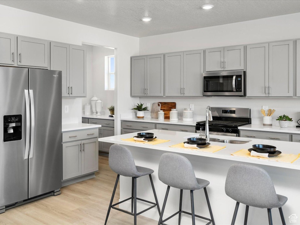 kitchen with light countertops, gray cabinets, a sink, appliances with stainless steel finishes, and a breakfast bar area