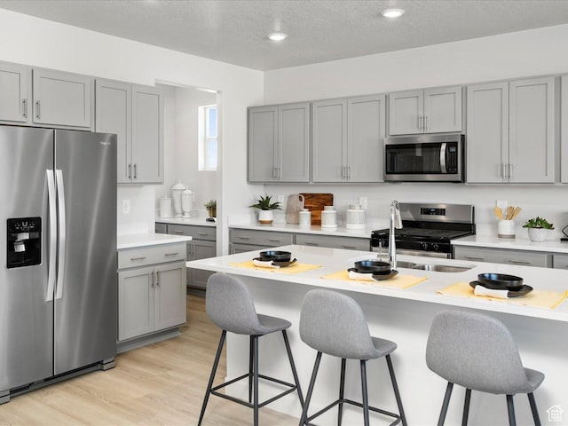 kitchen with light countertops, gray cabinets, a sink, appliances with stainless steel finishes, and a breakfast bar area