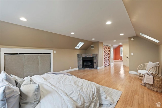 bedroom featuring a tile fireplace, light wood-style floors, lofted ceiling with skylight, visible vents, and baseboards