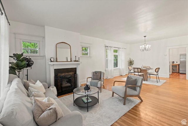 living area with an inviting chandelier, a fireplace with flush hearth, a healthy amount of sunlight, and light wood-style floors