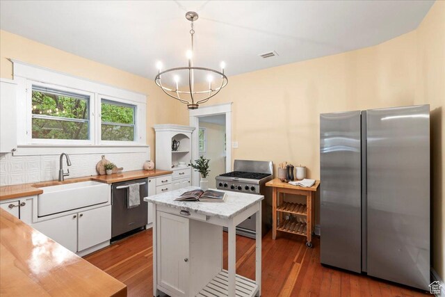 kitchen with appliances with stainless steel finishes, light countertops, a sink, white cabinetry, and a notable chandelier