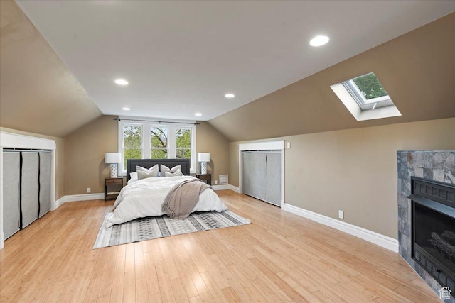 bedroom featuring vaulted ceiling with skylight, baseboards, recessed lighting, light wood finished floors, and a fireplace