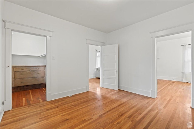 unfurnished bedroom featuring light wood-type flooring, a closet, baseboards, and a spacious closet