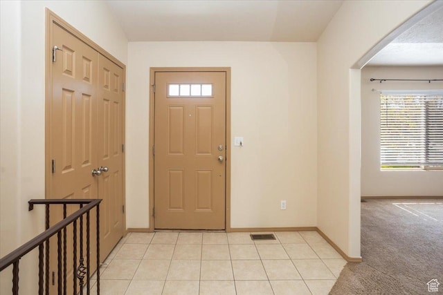entrance foyer featuring visible vents, light tile patterned floors, arched walkways, baseboards, and light colored carpet