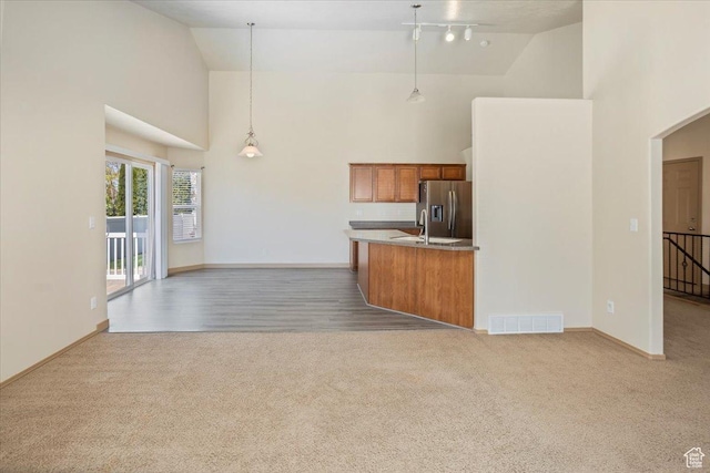 kitchen featuring visible vents, carpet, brown cabinets, stainless steel refrigerator with ice dispenser, and high vaulted ceiling