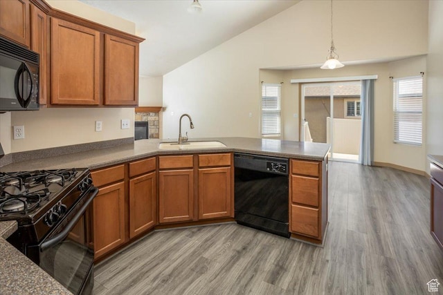 kitchen featuring a sink, light wood-style floors, black appliances, a peninsula, and brown cabinetry