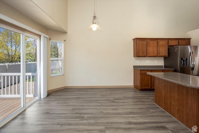 kitchen featuring brown cabinets, wood finished floors, baseboards, pendant lighting, and stainless steel refrigerator with ice dispenser