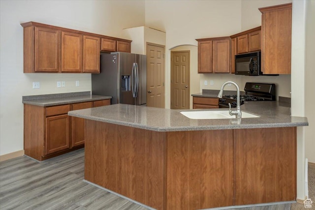 kitchen featuring range with gas stovetop, brown cabinetry, black microwave, light wood-style floors, and stainless steel fridge