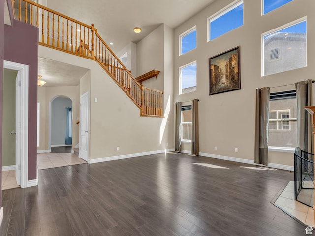 unfurnished living room featuring a high ceiling, arched walkways, wood finished floors, baseboards, and stairs