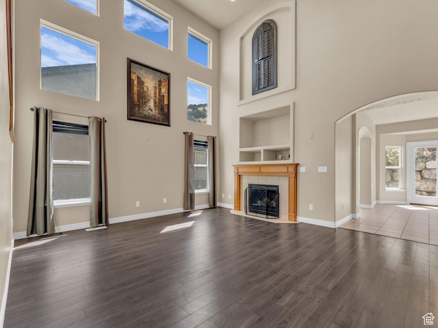 unfurnished living room with arched walkways, a high ceiling, dark wood finished floors, a fireplace, and built in shelves