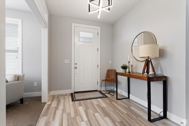 entryway featuring light wood-style flooring, baseboards, and a chandelier
