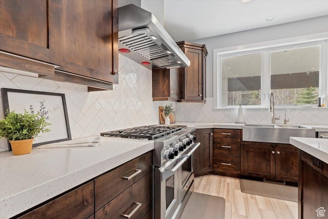 kitchen with double oven range, ventilation hood, a sink, backsplash, and dark brown cabinetry