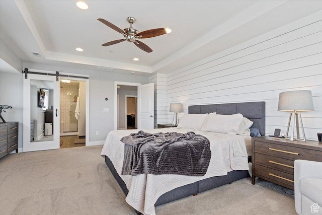 bedroom with a barn door, carpet flooring, recessed lighting, ensuite bath, and a tray ceiling