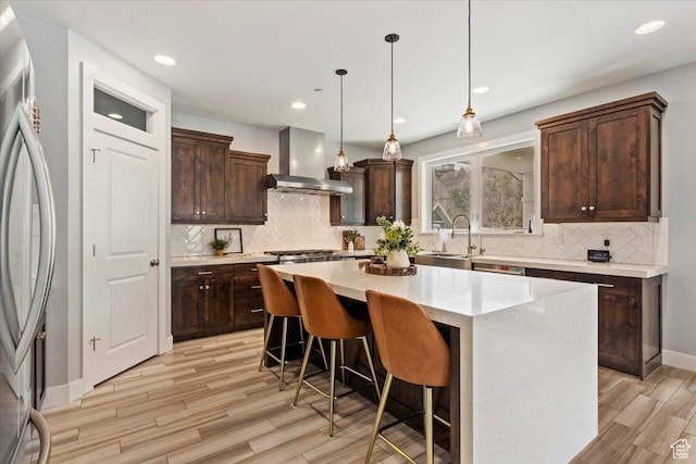 kitchen featuring wall chimney exhaust hood, a sink, stainless steel appliances, light wood finished floors, and dark brown cabinetry