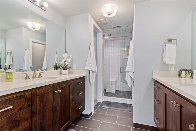 bathroom featuring tile patterned flooring, a stall shower, two vanities, and baseboards