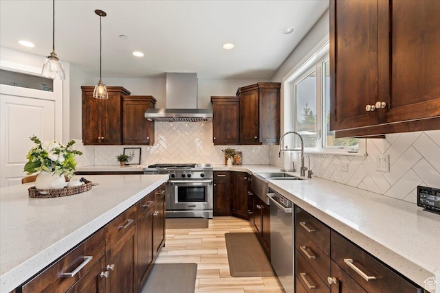 kitchen featuring wall chimney range hood, stainless steel appliances, a sink, light stone countertops, and recessed lighting