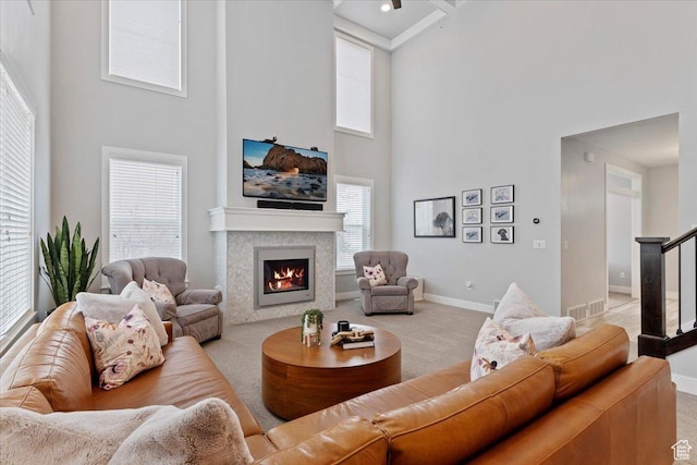 carpeted living area featuring a high ceiling, a lit fireplace, and baseboards