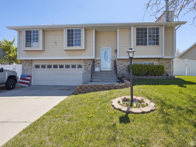 bi-level home featuring brick siding, an attached garage, fence, and a front yard