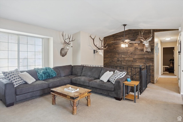 living room featuring wooden walls, a ceiling fan, vaulted ceiling, and carpet flooring