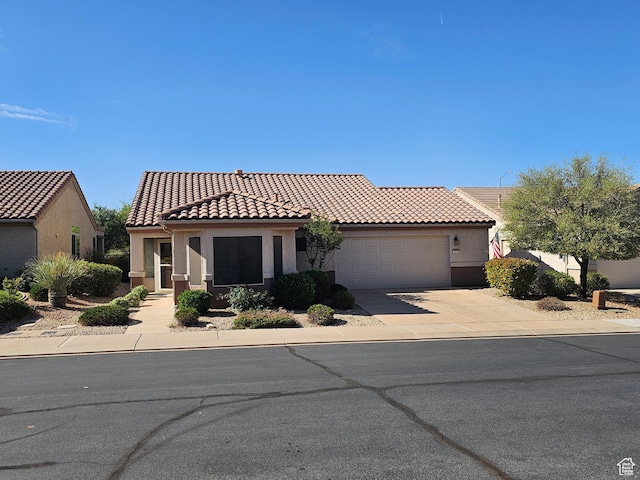 mediterranean / spanish-style home featuring concrete driveway, an attached garage, a tile roof, and stucco siding