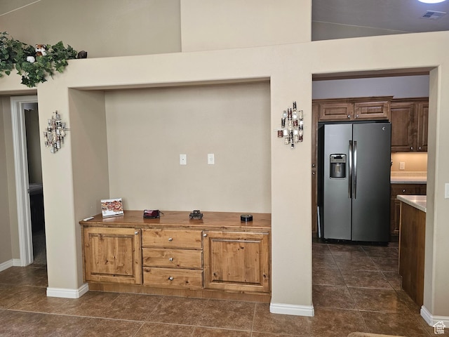 kitchen featuring stainless steel fridge with ice dispenser, dark tile patterned floors, visible vents, and baseboards