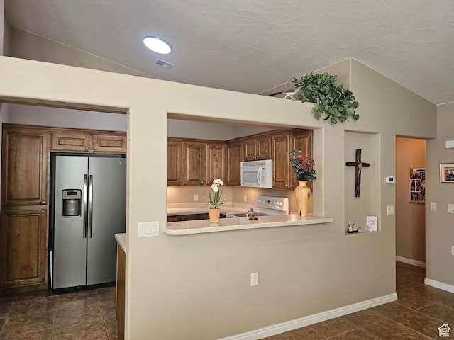 kitchen featuring vaulted ceiling, range with electric stovetop, stainless steel fridge with ice dispenser, white microwave, and light countertops