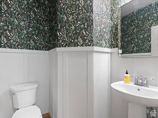 bathroom with a decorative wall, a sink, wallpapered walls, a wainscoted wall, and toilet