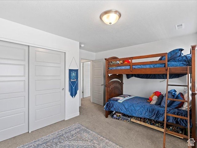 bedroom featuring carpet flooring, a textured ceiling, visible vents, and a closet
