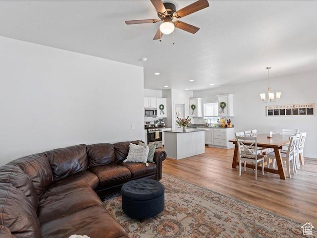 living room with recessed lighting, light wood-type flooring, and ceiling fan with notable chandelier