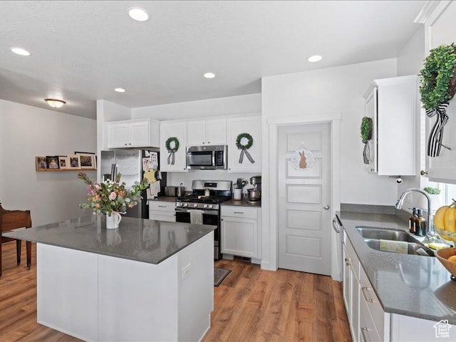 kitchen featuring recessed lighting, stainless steel appliances, wood finished floors, a sink, and white cabinetry