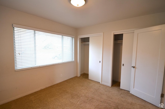 unfurnished bedroom featuring light carpet, multiple closets, and baseboards