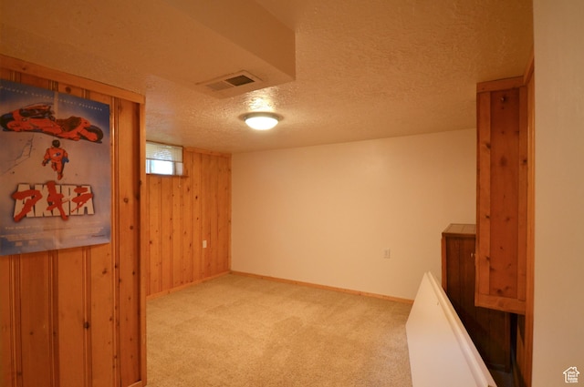 basement with carpet flooring, a textured ceiling, visible vents, baseboards, and wood walls