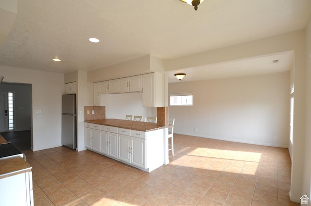 kitchen with white cabinets, freestanding refrigerator, light tile patterned floors, and recessed lighting