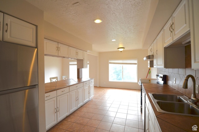 kitchen with tile counters, a textured ceiling, electric range, under cabinet range hood, and freestanding refrigerator
