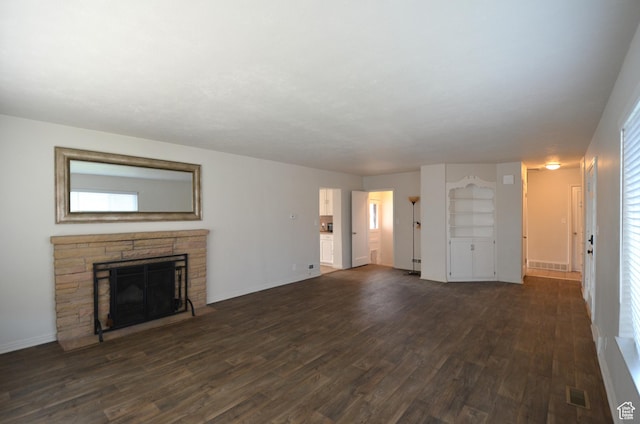 unfurnished living room with dark wood-style floors, a stone fireplace, and visible vents