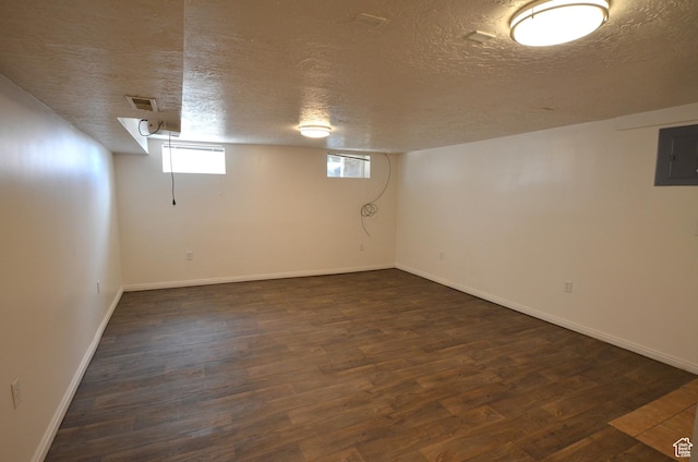 below grade area with dark wood-type flooring, a textured ceiling, electric panel, and visible vents