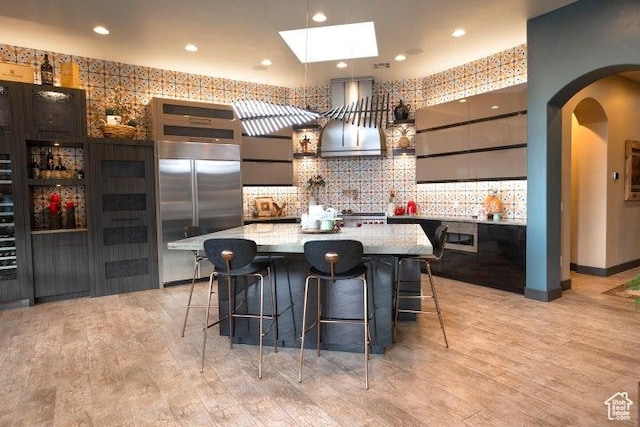 3052 N Snow Canyon Pkwy Unit 67, St George, UT 84770 - kitchen featuring arched walkways, built in refrigerator, wall chimney exhaust hood, a skylight, and a kitchen bar