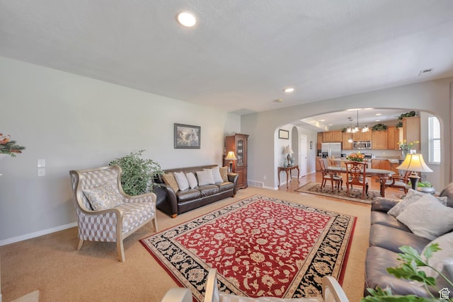 living room with recessed lighting, an inviting chandelier, light carpet, arched walkways, and baseboards