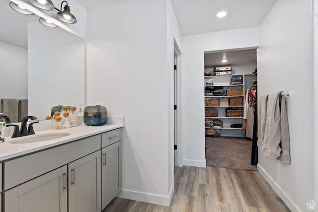 full bathroom with a spacious closet, baseboards, vanity, and wood finished floors