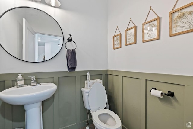 half bath with a decorative wall, a wainscoted wall, a sink, and toilet